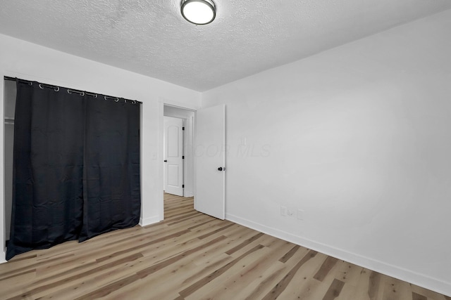 unfurnished bedroom featuring light wood-style floors, a textured ceiling, and baseboards