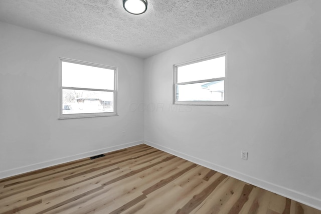 unfurnished room featuring light wood-style flooring, plenty of natural light, visible vents, and baseboards