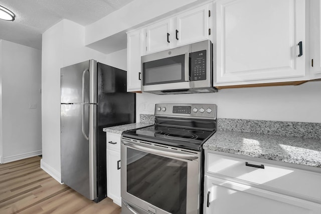 kitchen with a textured ceiling, light stone counters, white cabinets, appliances with stainless steel finishes, and light wood-type flooring