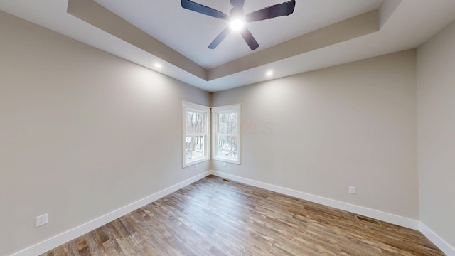 empty room featuring a tray ceiling, ceiling fan, and wood-type flooring