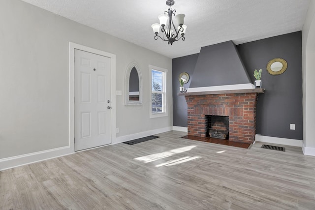 unfurnished living room featuring a textured ceiling, light wood-type flooring, a fireplace, and an inviting chandelier