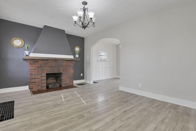 unfurnished living room featuring an inviting chandelier, light hardwood / wood-style floors, a textured ceiling, and a brick fireplace