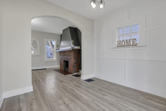 unfurnished living room featuring light hardwood / wood-style flooring, a chandelier, and a brick fireplace