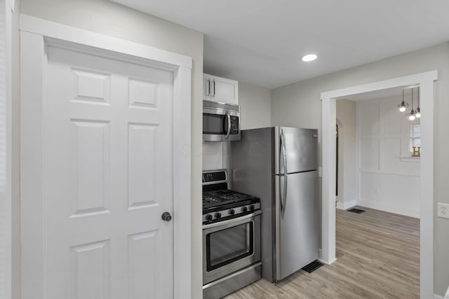 kitchen featuring appliances with stainless steel finishes, light wood-type flooring, decorative light fixtures, an inviting chandelier, and white cabinets