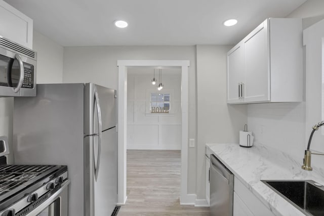 kitchen with light stone countertops, sink, stainless steel appliances, white cabinets, and light wood-type flooring