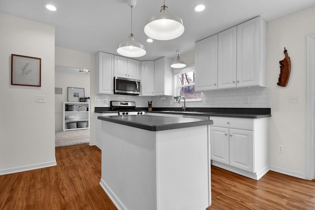 kitchen featuring tasteful backsplash, stainless steel appliances, pendant lighting, hardwood / wood-style flooring, and white cabinetry