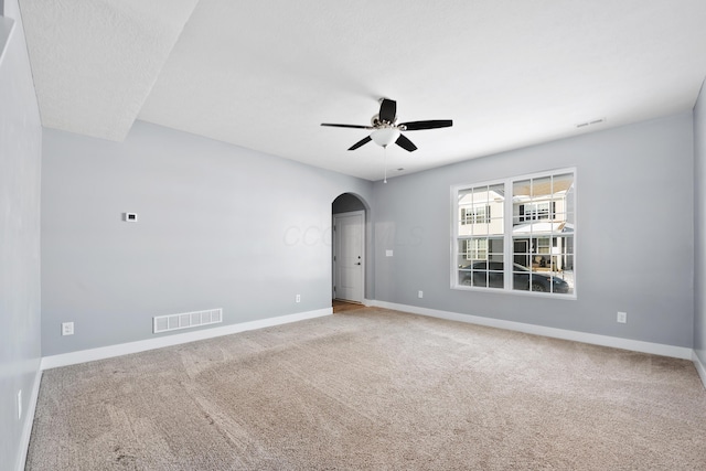 carpeted spare room featuring ceiling fan, baseboards, visible vents, and arched walkways