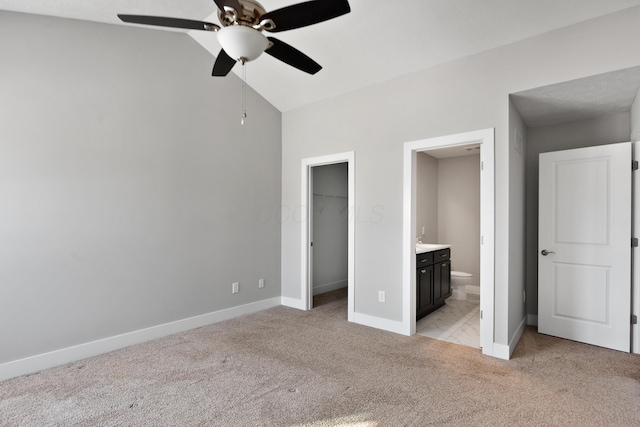 unfurnished bedroom featuring light carpet, baseboards, ensuite bathroom, a walk in closet, and a closet