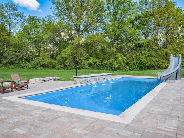 view of pool featuring pool water feature, a patio, a water slide, and a lawn