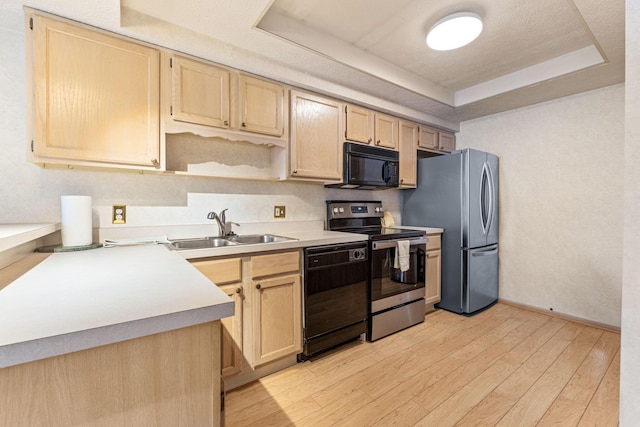 kitchen with a raised ceiling, light wood-style floors, light brown cabinetry, black appliances, and a sink