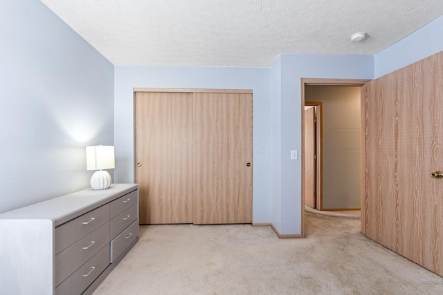 unfurnished bedroom featuring a textured ceiling, a closet, baseboards, and light colored carpet