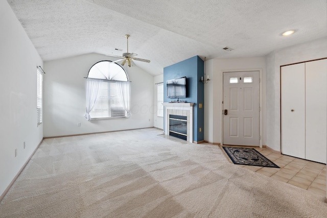 unfurnished living room with a tile fireplace, ceiling fan, vaulted ceiling, a textured ceiling, and carpet floors