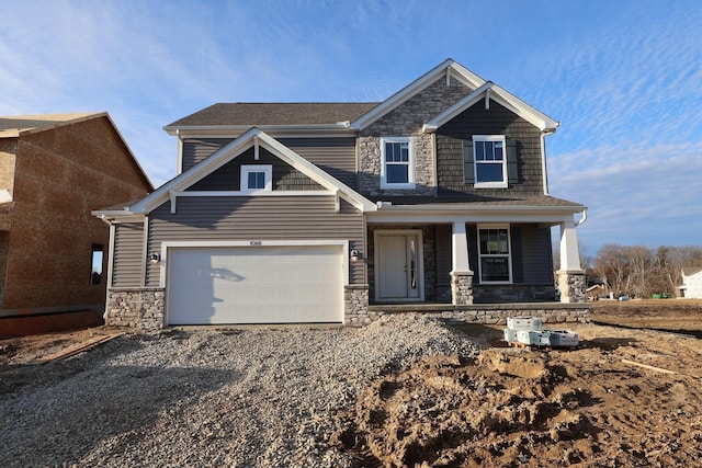 craftsman-style house with covered porch, stone siding, and gravel driveway