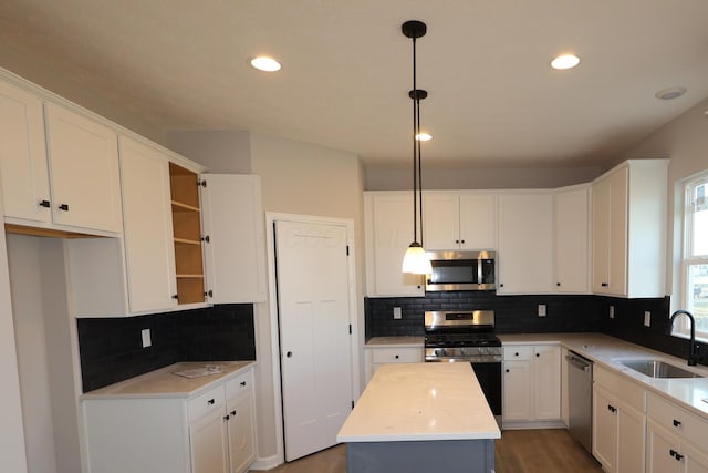 kitchen featuring appliances with stainless steel finishes, a center island, light countertops, white cabinetry, and a sink