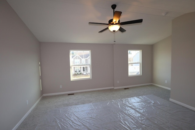 carpeted spare room featuring baseboards, visible vents, and ceiling fan