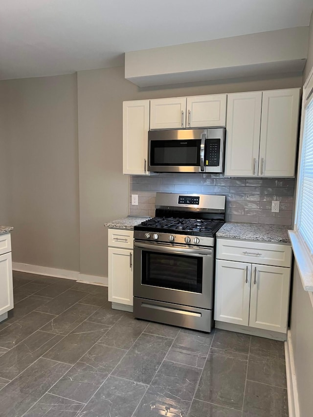 kitchen with white cabinetry, light stone countertops, appliances with stainless steel finishes, and backsplash