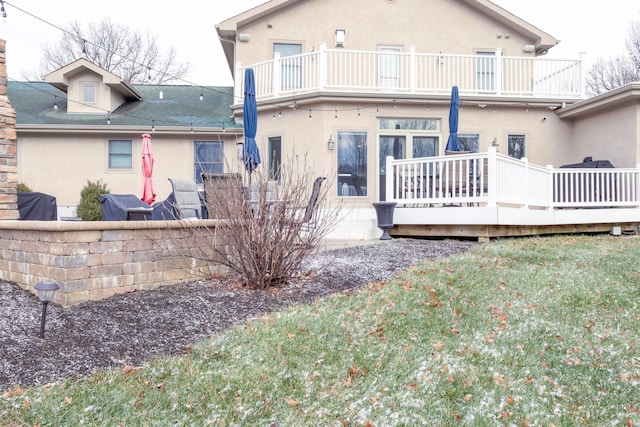 back of property featuring stucco siding, a lawn, a balcony, and a shingled roof