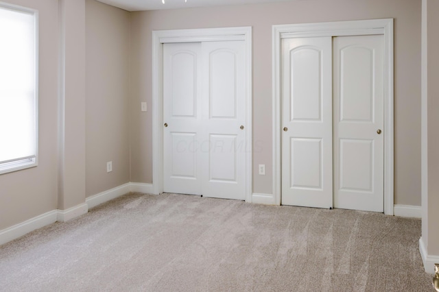 unfurnished bedroom featuring baseboards, multiple closets, and carpet