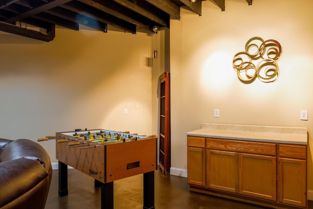 playroom featuring baseboards, beam ceiling, and finished concrete flooring