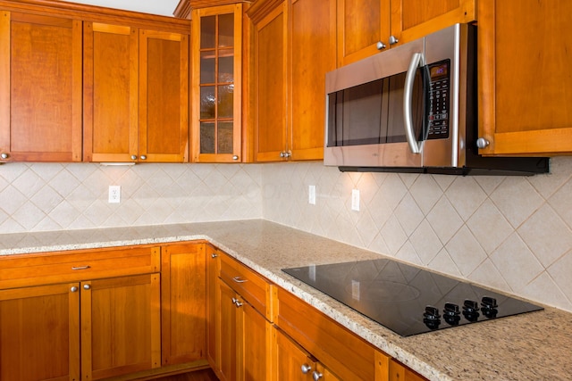 kitchen featuring light stone counters, stainless steel microwave, glass insert cabinets, and black electric cooktop