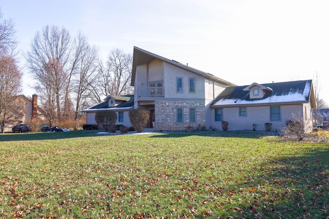 rear view of property featuring stucco siding, stone siding, a balcony, and a lawn