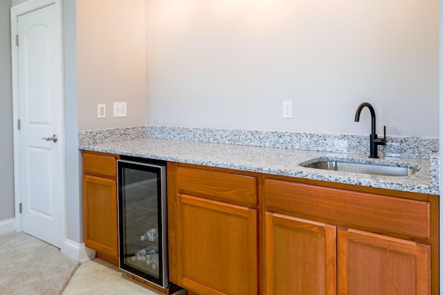 kitchen featuring a sink, light stone countertops, brown cabinets, and beverage cooler