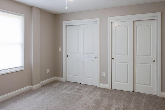 unfurnished bedroom with baseboards, two closets, and carpet