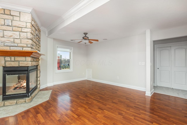 unfurnished living room featuring a stone fireplace, crown molding, wood finished floors, and baseboards