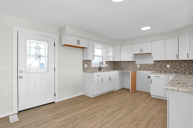 kitchen featuring backsplash, light stone counters, sink, light hardwood / wood-style flooring, and white cabinets