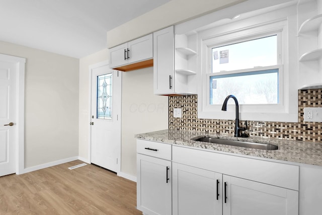 kitchen with white cabinets, decorative backsplash, light stone countertops, and sink