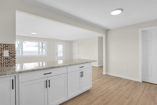 kitchen featuring kitchen peninsula, white cabinetry, light hardwood / wood-style flooring, and light stone counters