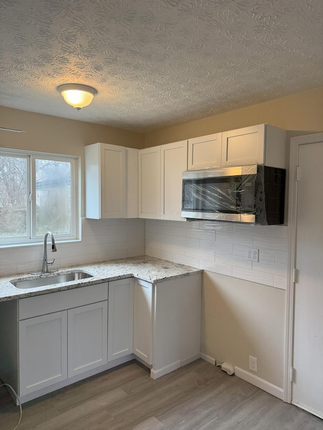 kitchen with light stone countertops, light hardwood / wood-style floors, white cabinetry, and sink