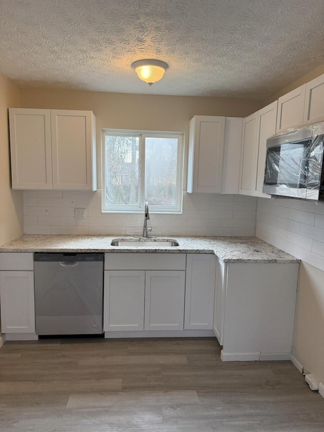 kitchen with sink, light hardwood / wood-style flooring, stainless steel dishwasher, backsplash, and white cabinets