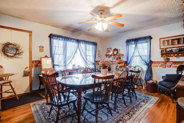 dining room featuring wood-type flooring, a textured ceiling, ceiling fan, and a healthy amount of sunlight