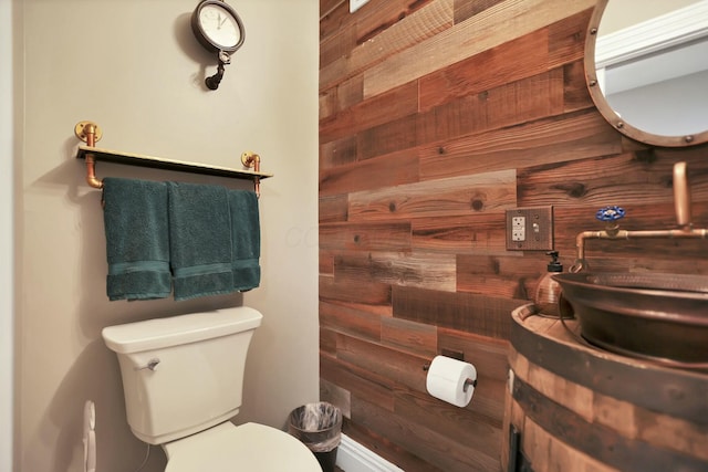 bathroom with toilet, wooden walls, and sink