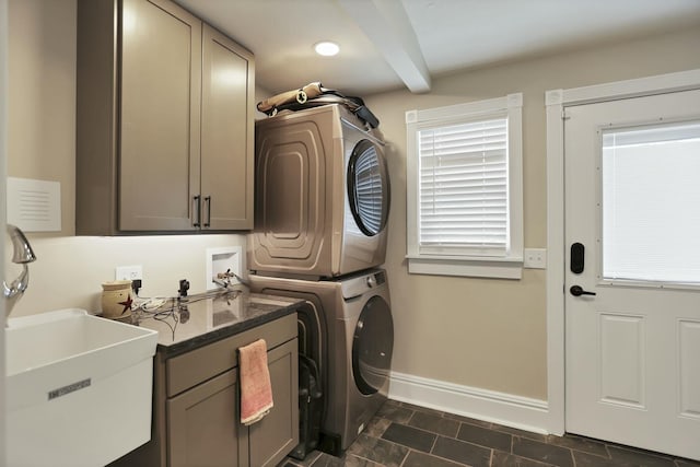 clothes washing area featuring sink, cabinets, and stacked washer / dryer