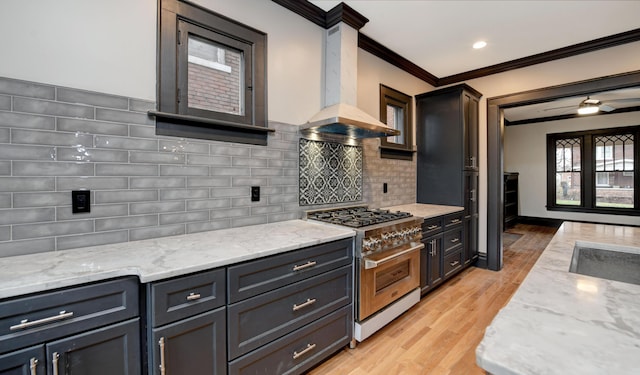 kitchen with stainless steel range, light stone counters, light hardwood / wood-style floors, decorative backsplash, and exhaust hood