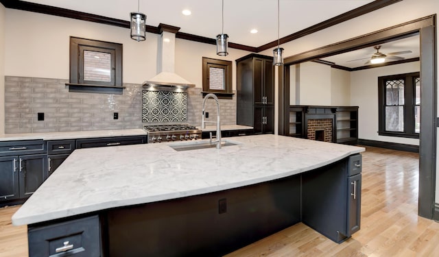 kitchen featuring pendant lighting, a center island with sink, wall chimney range hood, ceiling fan, and tasteful backsplash