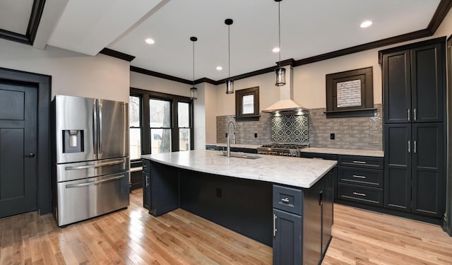 kitchen featuring stainless steel fridge, backsplash, a kitchen island with sink, light hardwood / wood-style flooring, and hanging light fixtures