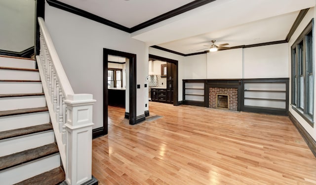 unfurnished living room with light hardwood / wood-style floors, a brick fireplace, ceiling fan, and crown molding