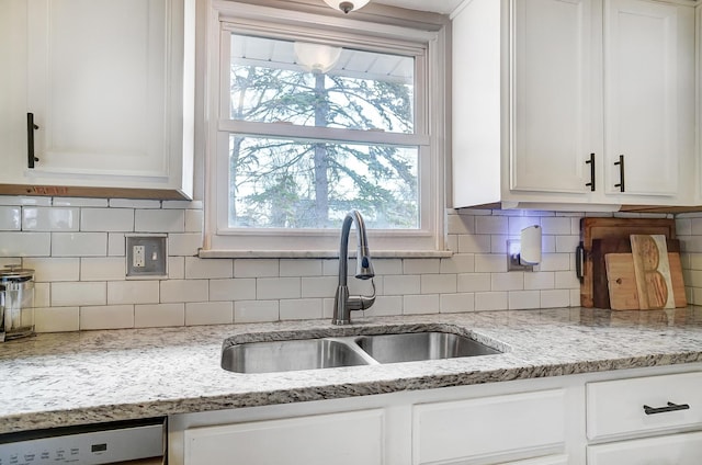 kitchen with light stone counters, dishwasher, sink, and white cabinets