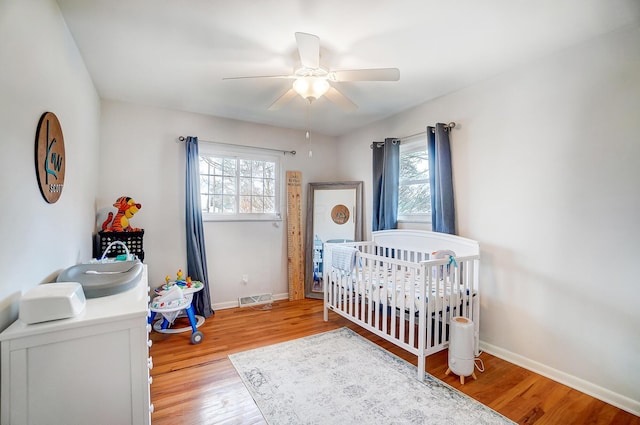 bedroom featuring ceiling fan, light hardwood / wood-style flooring, and a crib