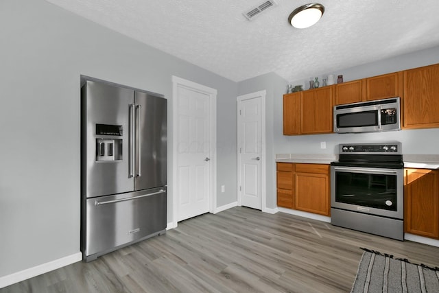 kitchen featuring light wood-type flooring, a textured ceiling, and appliances with stainless steel finishes