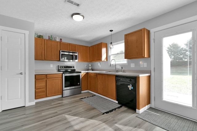 kitchen featuring sink, light hardwood / wood-style floors, pendant lighting, a textured ceiling, and appliances with stainless steel finishes