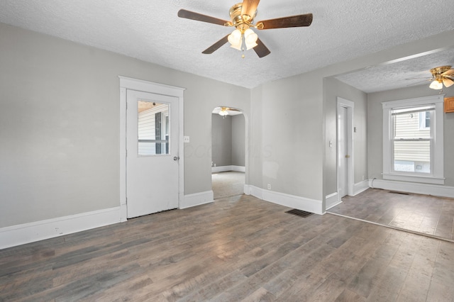 empty room featuring baseboards, arched walkways, a ceiling fan, wood finished floors, and a textured ceiling