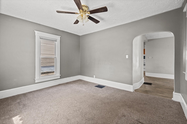 carpeted spare room with arched walkways, ceiling fan, a textured ceiling, visible vents, and baseboards