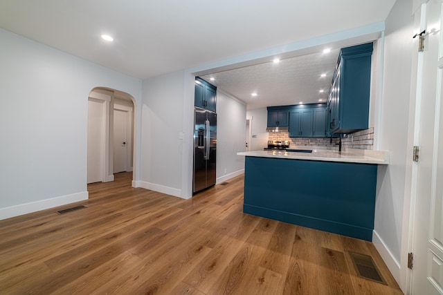 kitchen featuring kitchen peninsula, decorative backsplash, stainless steel fridge with ice dispenser, and blue cabinetry