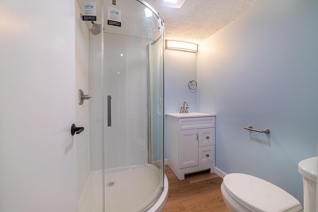 bathroom featuring vanity, hardwood / wood-style flooring, toilet, a textured ceiling, and a shower with shower door