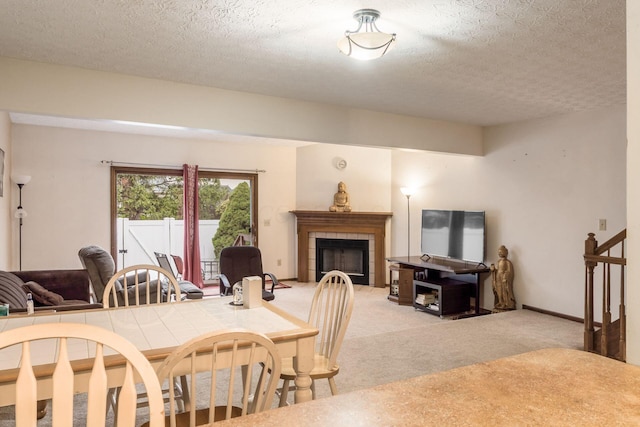 dining area featuring a tile fireplace, light carpet, and a textured ceiling