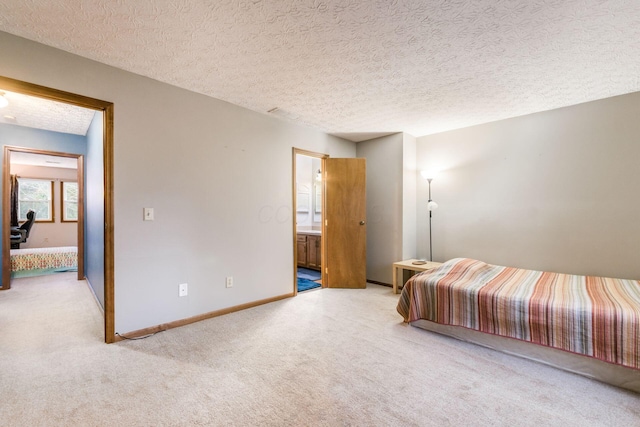 bedroom with ensuite bathroom, light colored carpet, and a textured ceiling